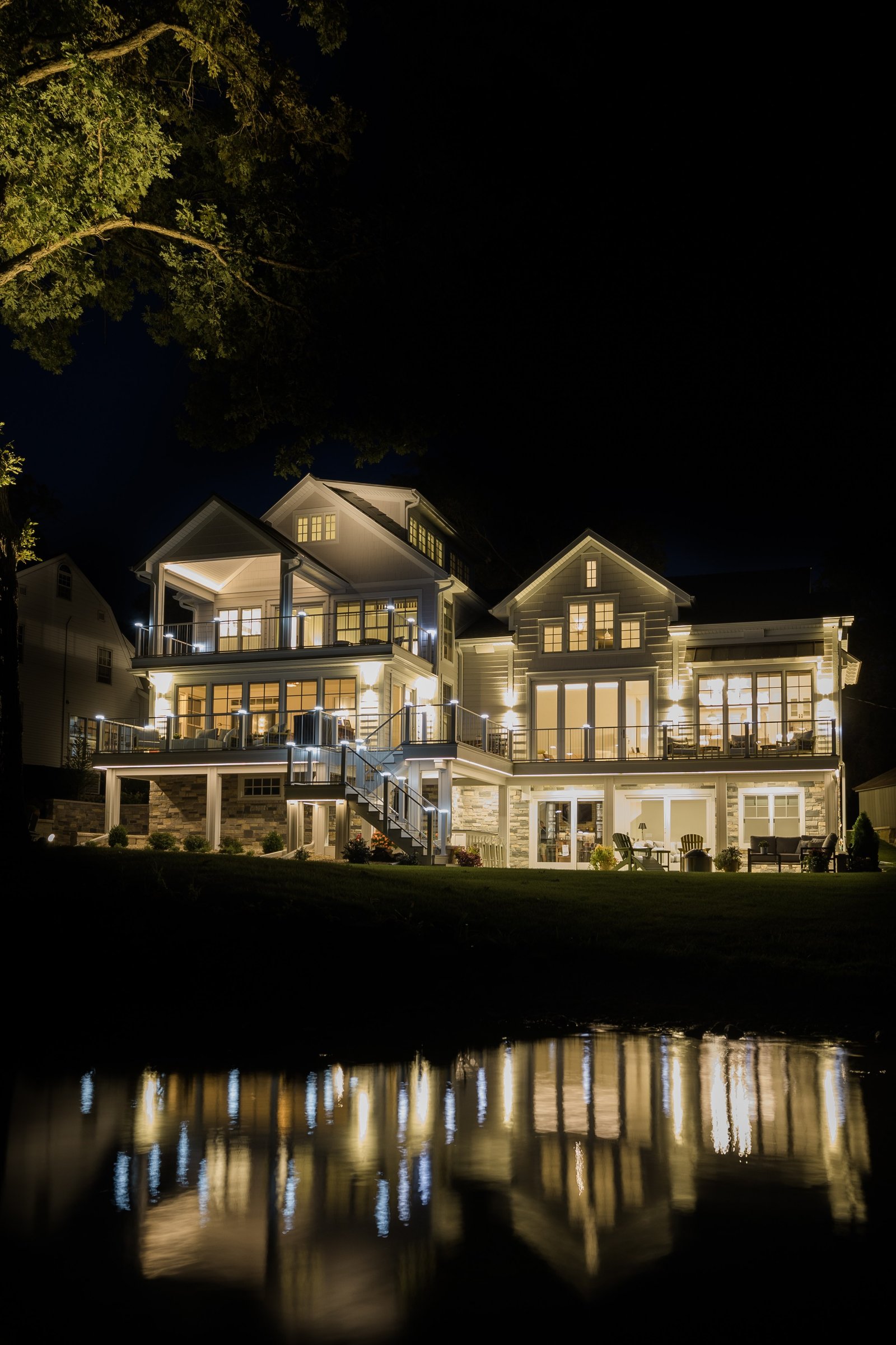 Night view of the lit lakehouse from the shoreline, its lights reflected in the dark water below