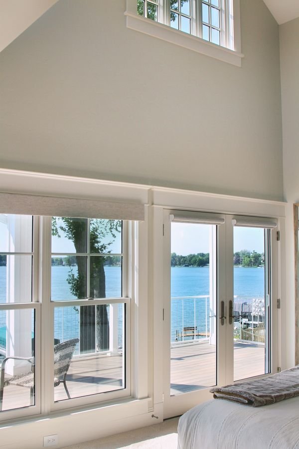 Vaulted bedroom with tall windows and French doors opening to a deck over the lake