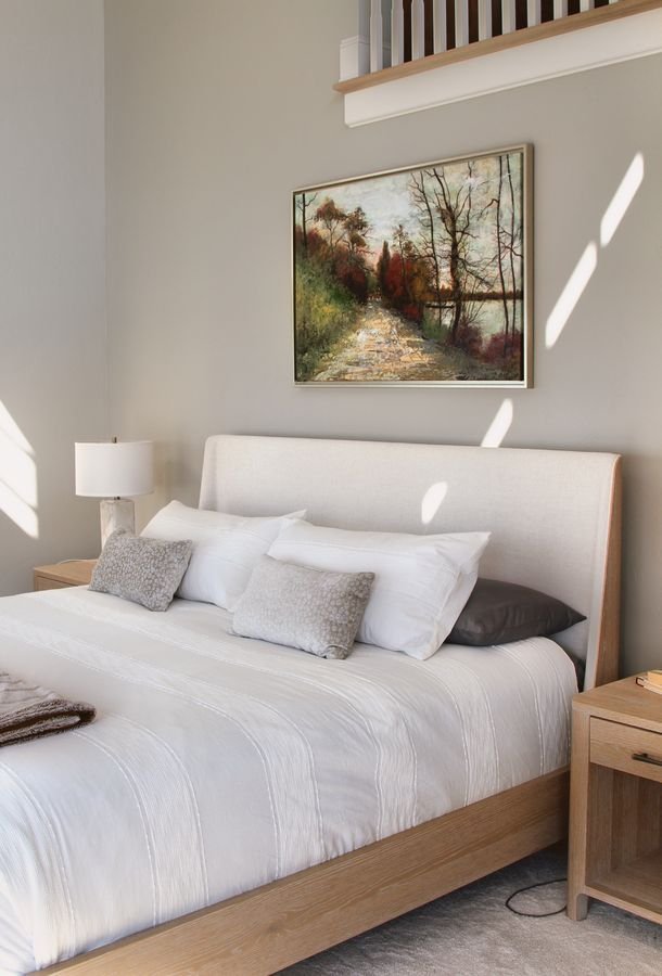 Bedroom with an upholstered bed, a landscape painting, and the loft railing above