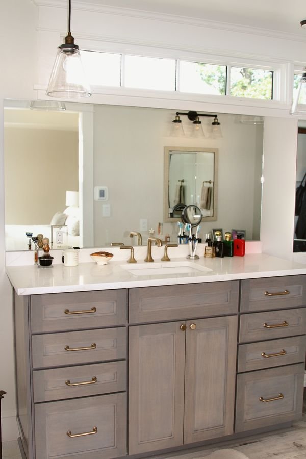 Gray double vanity with brass hardware, a white countertop, and transom windows above the mirror