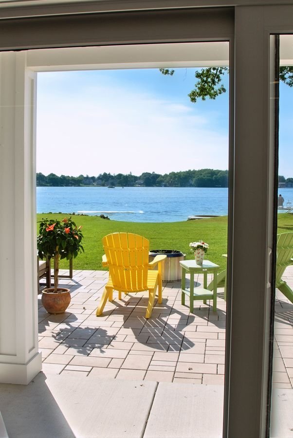 View through the walkout opening to the patio, Adirondack chairs on the lawn, and the lake beyond