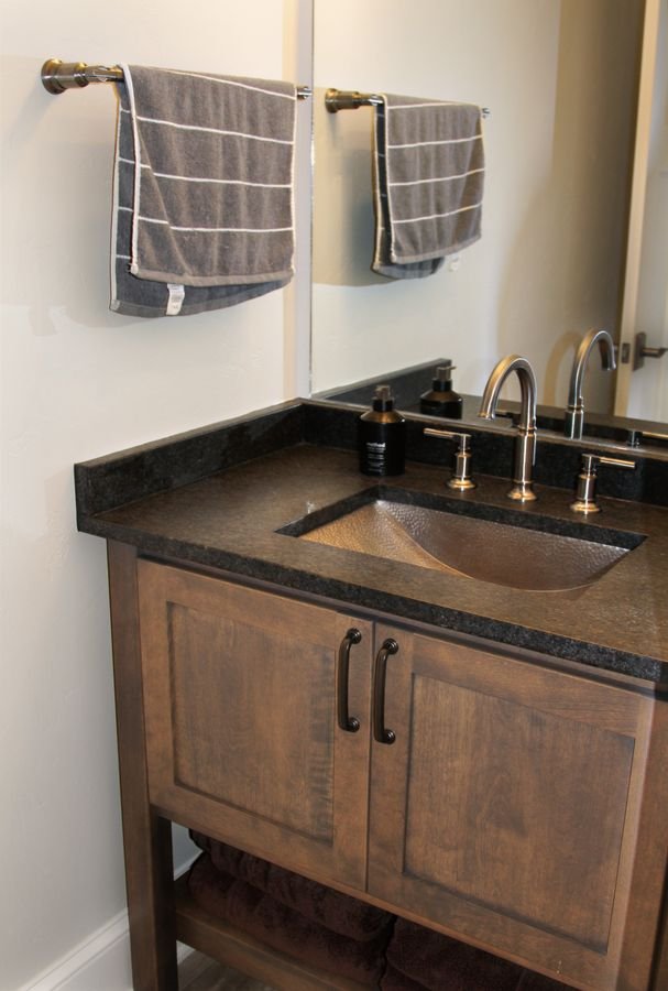 Dark wood vanity with a hammered metal sink and a dark stone countertop