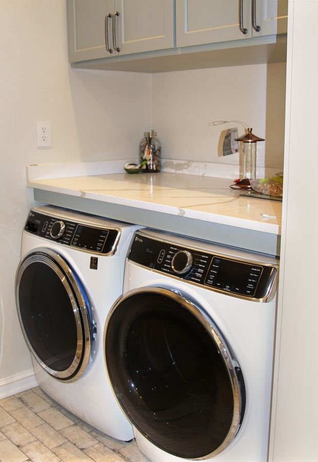 Laundry with front-load washer and dryer beneath a stone countertop and upper cabinets