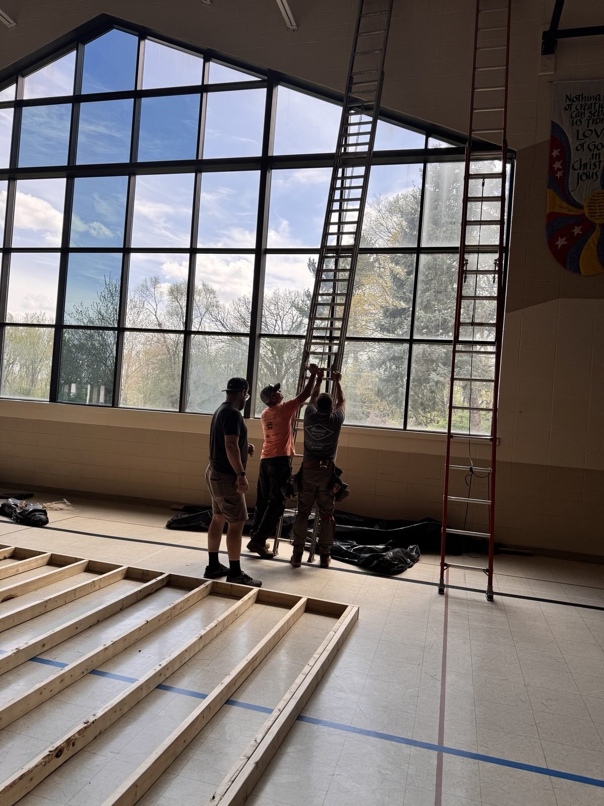The Monien crew raising a tall ladder against the gym windows at Our Redeemer Lutheran Church during the stage build