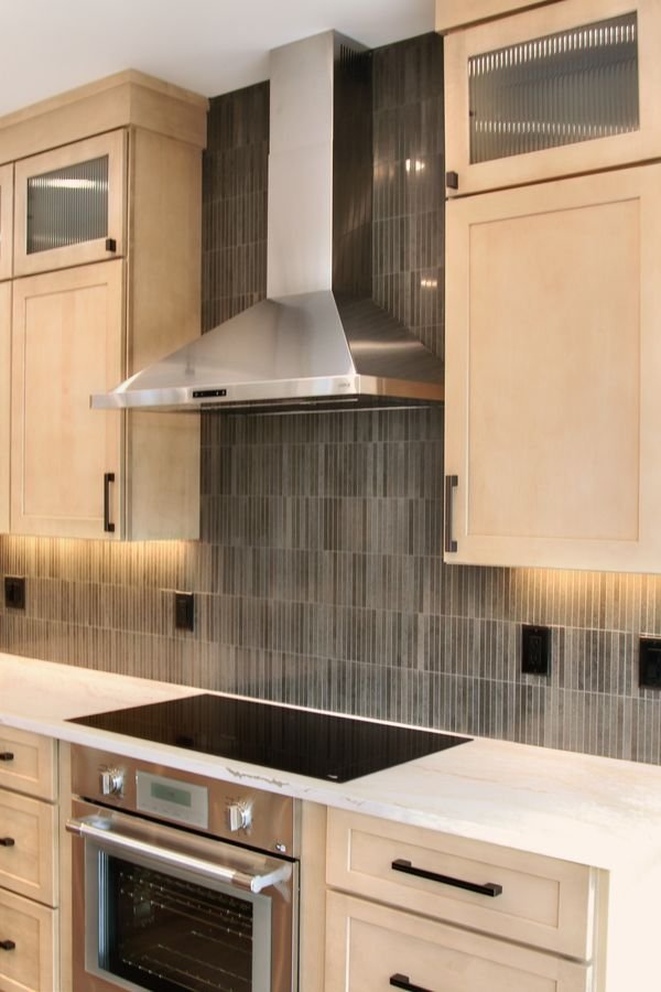 Induction cooktop beneath a stainless hood against floor-to-ceiling dark tile