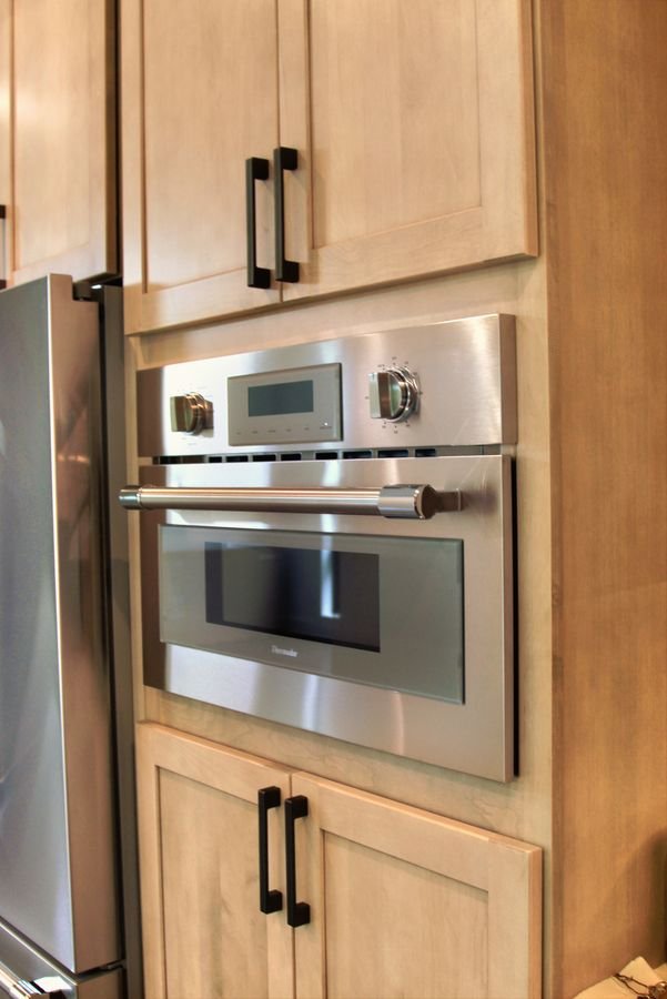 Stainless wall oven built into maple cabinetry with black pulls