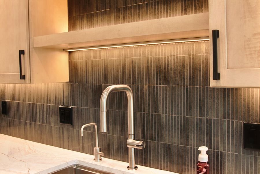 Brushed faucet and filtered water tap against a dark tile backsplash with lit floating shelves