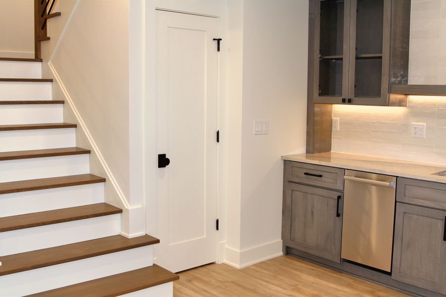 Lower level stair beside the drop zone with gray cabinetry and an undercounter appliance