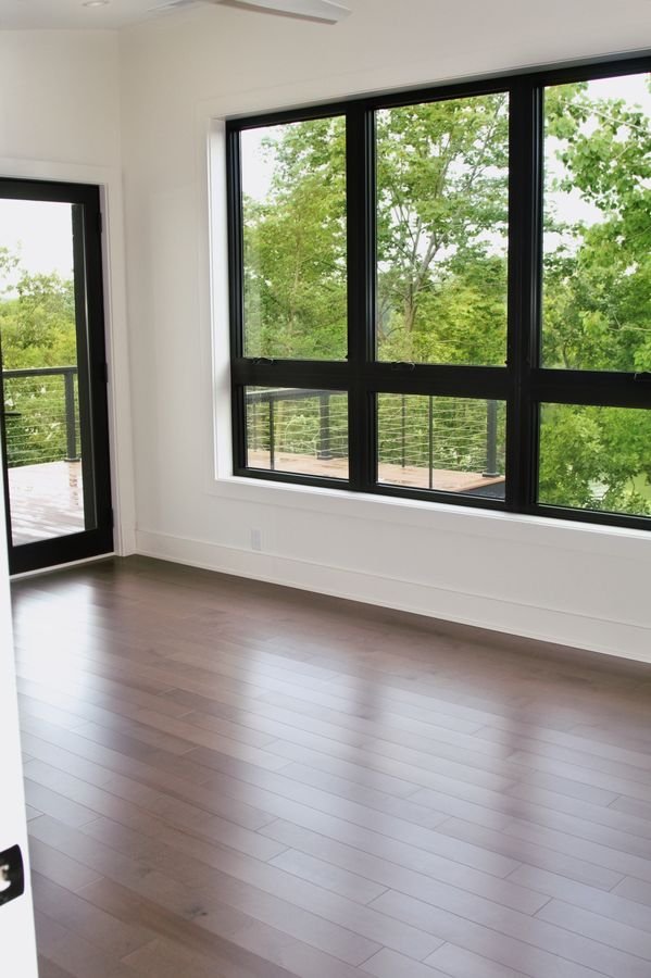 Bedroom with black-framed windows and a door to the deck, looking into the trees