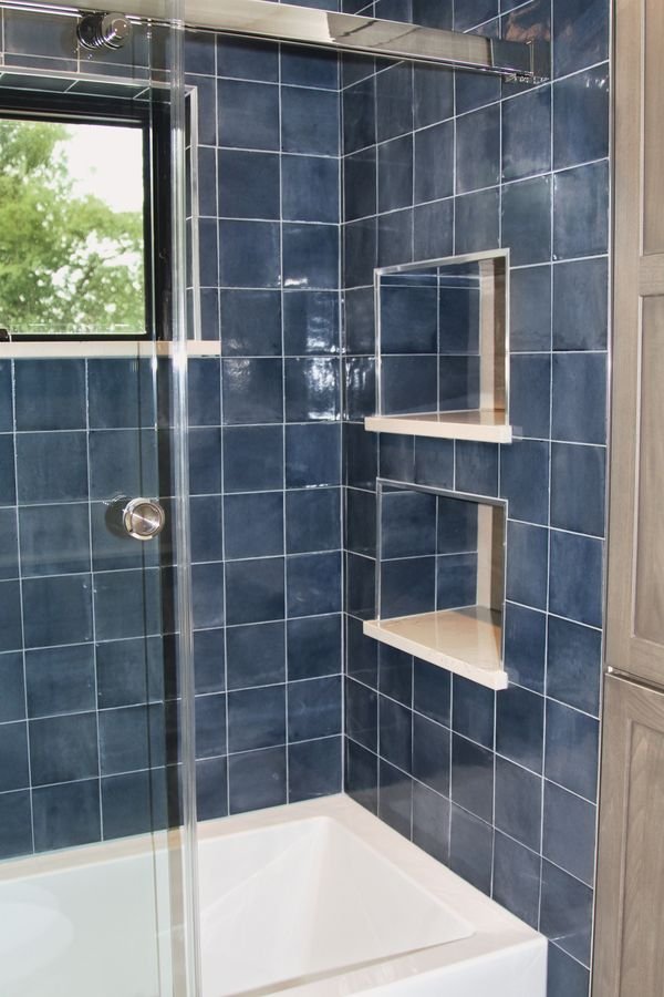 Tub and shower in glazed blue tile with recessed niches and a glass door