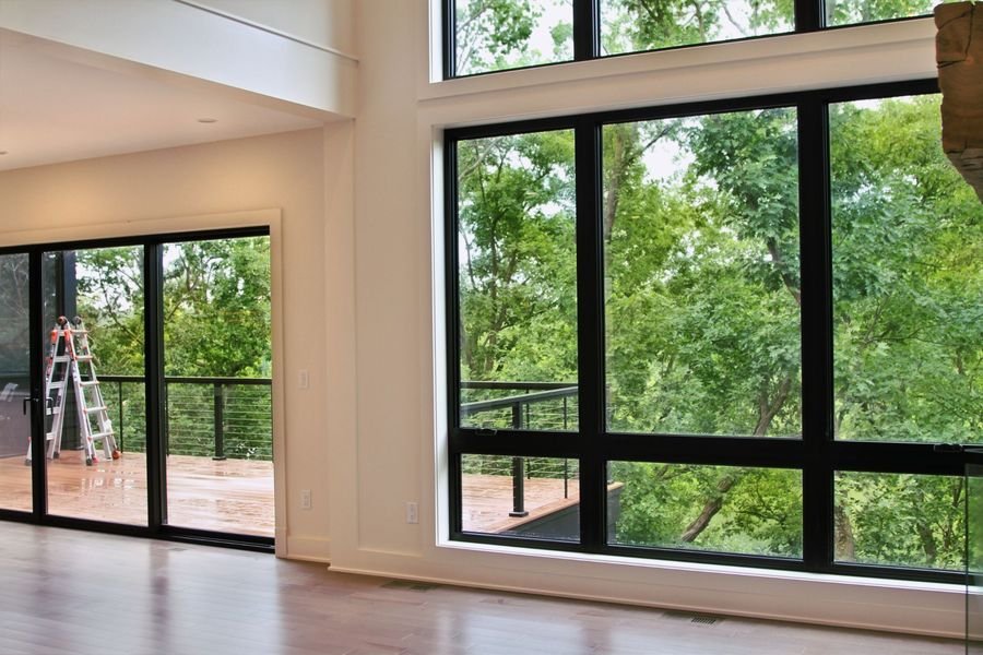 Two-story black-framed window wall opening to the deck, with the trees and lake beyond